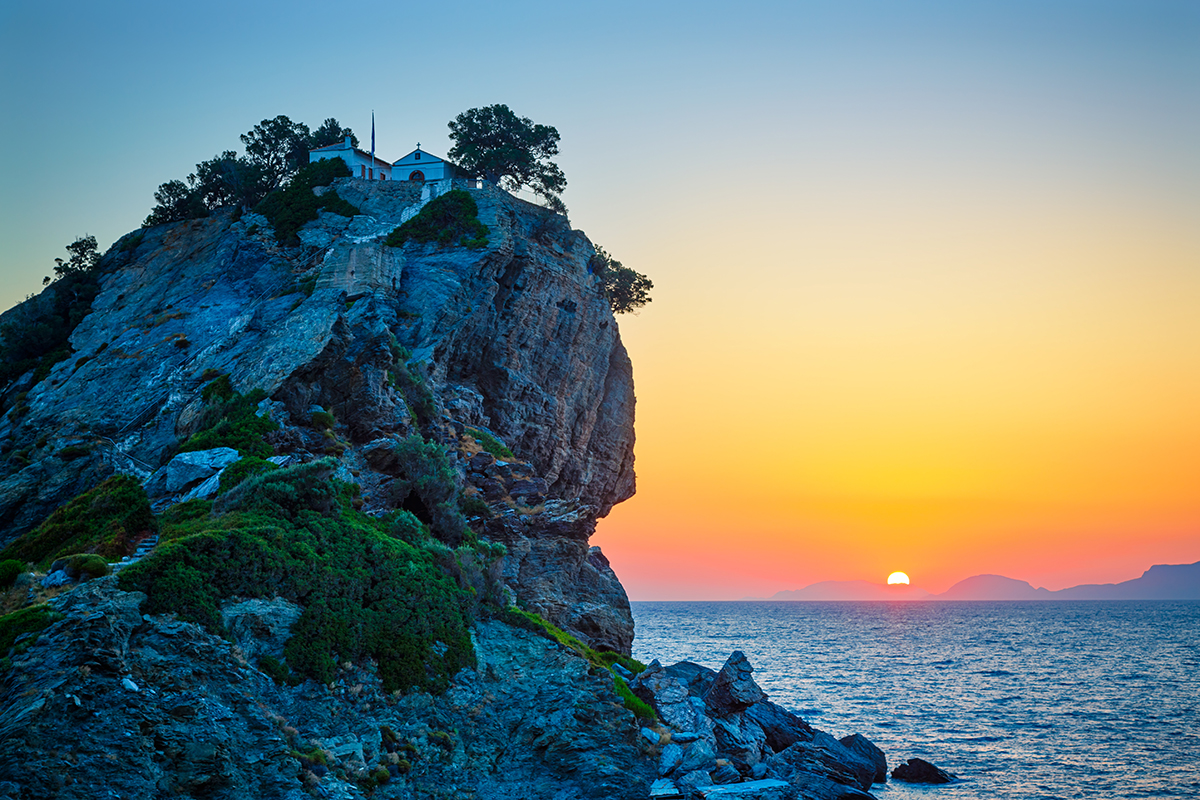 Rock with famous church Agios Ioannis Kastri on Skopelos island Greece at sunrise where scenes of Mamma Mia movie were filmed Sun raises above Alonissos island