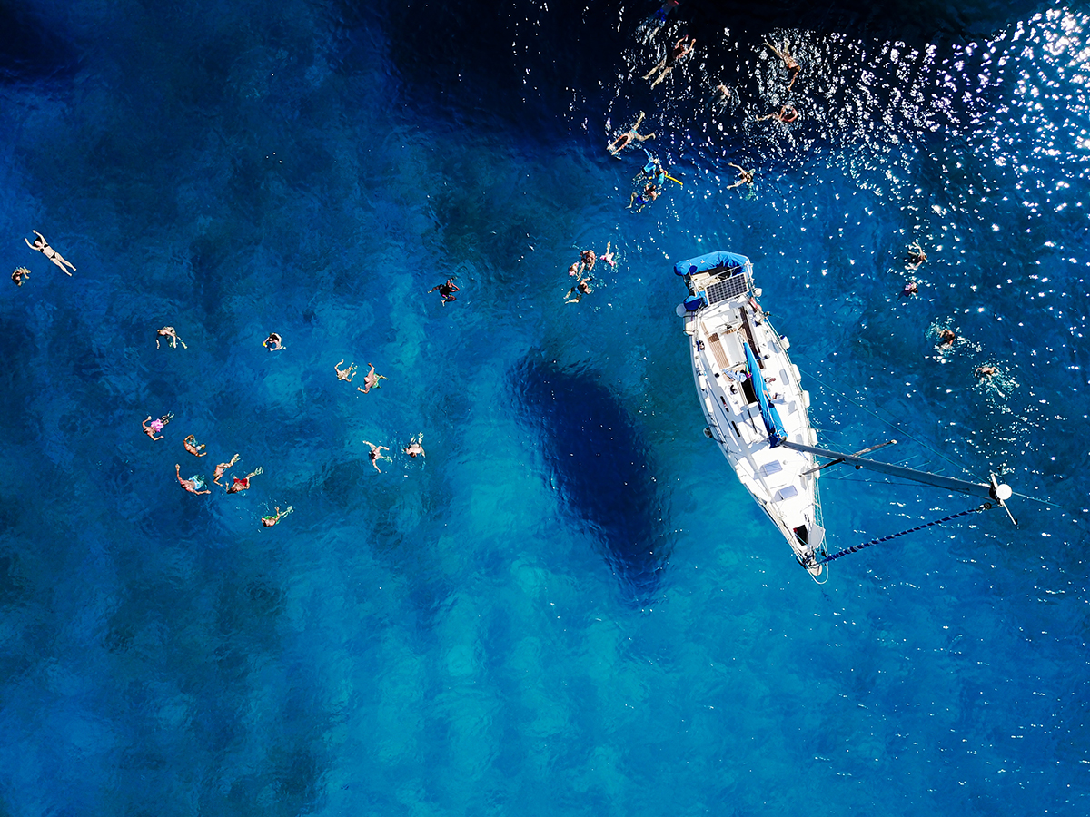 Aerial shot of beautiful blue lagoon at hot summer day with sailing boat Top view of people are swimming around the boat